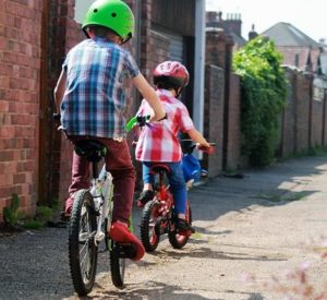 two young children riding bicycles with helmets on in alley Queener Law