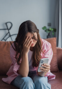 A woman looking at her smartphone, representing the emotional distress and privacy concerns that can arise when private images or videos are shared online without consent.